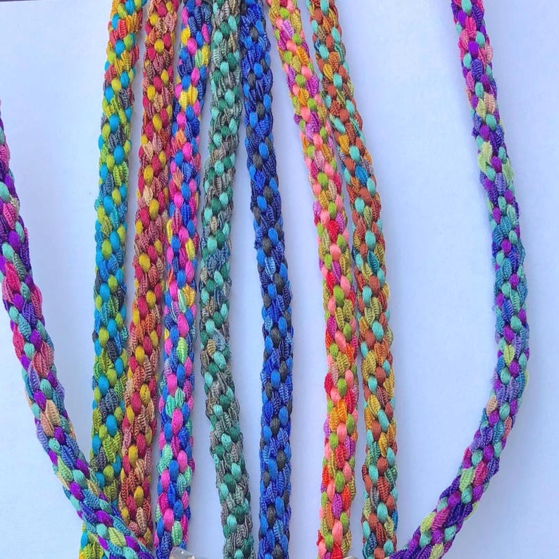 May include: A collection of multiple braided cords featuring a vibrant array of colors including pink, blue, green, yellow, and orange. Each cord is constructed from tightly woven threads, creating a textured, cylindrical appearance throughout.
