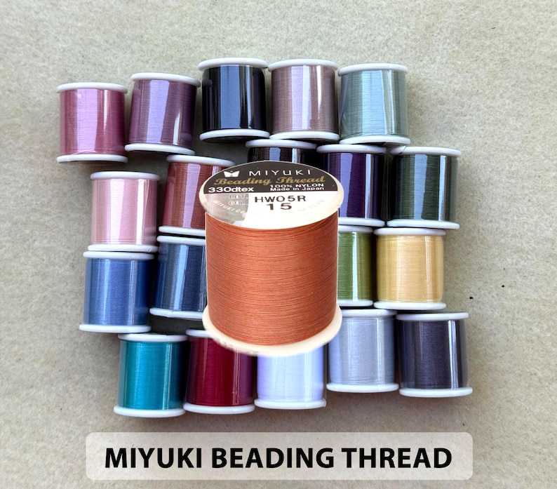 May include: A collection of colorful Miyuki beading thread spools. The spools are in various colors, including pink, blue, purple, and green. The text "MIYUKI BEADING THREAD" is displayed at the bottom of the image.