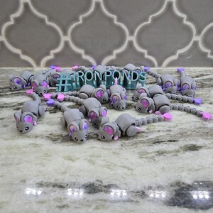 May include: A collection of gray mouse figurines with pink and purple accents. The mice are arranged on a marble surface, with the text "#IRONPONDS" in the background. The figurines have detailed features, including ears and tails.