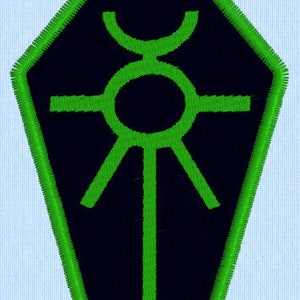 Könnte beinhalten: Ein grüner und schwarzer gestickter Aufnäher in Form eines Sarges mit einem stilisierten Sonnensymbol im Inneren.