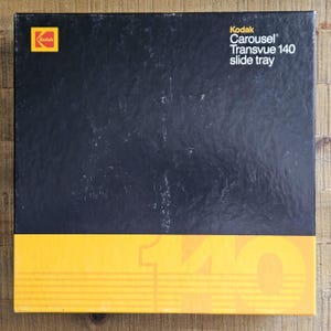 May include: A black Kodak Carousel Transvue 140 slide tray box. The box has a yellow stripe at the bottom with the number 140. The Kodak logo is in the upper left corner.