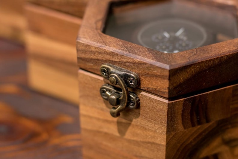 K&ouml;nnte beinhalten: Eine sechseckige Holzkiste mit Glasdeckel. Die Kiste hat einen Messingverschluss und ist aus dunklem Holz gefertigt.