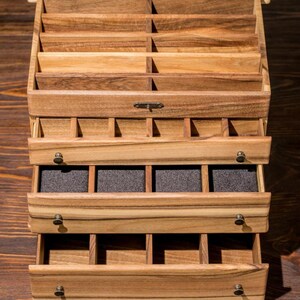 May include: A wooden box with multiple drawers, each with compartments. The drawers are open, revealing the compartments inside. The box is made of light brown wood with a natural finish.