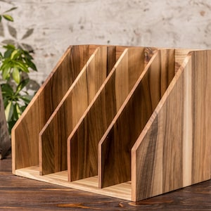 May include: Wooden magazine rack with five compartments, made of light brown wood with a natural wood grain finish.