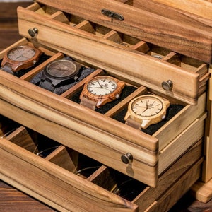 May include: Wooden watch box with multiple drawers. The drawers are open and reveal several wooden watches with different colored bands.