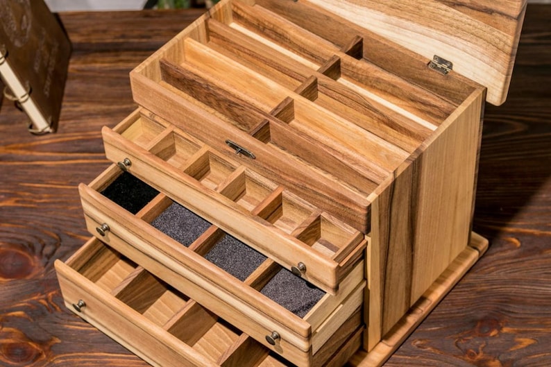 May include: Wooden jewelry box with multiple drawers and compartments. The box is made of light brown wood with a natural finish. The drawers are lined with black felt.