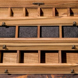 May include: A wooden jewelry box with three drawers. The top drawer has multiple compartments, the middle drawer has four compartments lined with black felt, and the bottom drawer has multiple compartments.