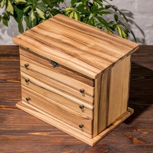 May include: A wooden jewelry box with four drawers and a hinged lid. The box is made of light brown wood with a natural wood finish. The drawers have small metal handles.