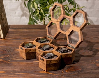 Op de afbeelding: Een houten horlogebox met een honingraatontwerp. De deksel is open en de doos heeft zes vakken om horloges op te bergen. Elk vak heeft een zachte, zwarte voering om de horloges te beschermen.