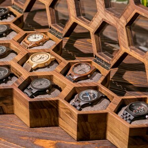 K&ouml;nnte beinhalten: Eine Holzuhrbox mit einem Wabenmuster. Die Box ist ge&ouml;ffnet und enth&auml;lt neun Uhren mit verschiedenen Armb&auml;ndern und Zifferbl&auml;ttern.