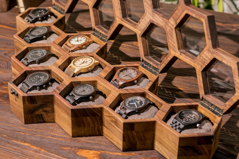 K&ouml;nnte beinhalten: Eine Holzuhrbox mit einem Wabenmuster. Die Box ist ge&ouml;ffnet und enth&auml;lt neun Uhren mit verschiedenen Armb&auml;ndern und Zifferbl&auml;ttern.