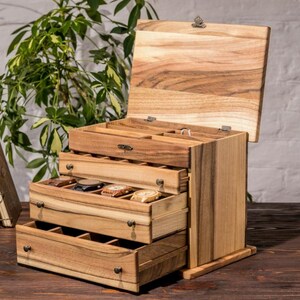 May include: A wooden watch box with a hinged lid and three drawers. The box is made of light brown wood with a natural wood grain. The drawers are open and reveal compartments for storing watches.
