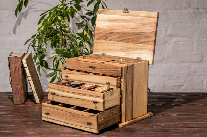 May include: A wooden watch box with a hinged lid and three drawers. The box is made of light brown wood with a natural wood grain. The drawers are open and reveal compartments for storing watches.