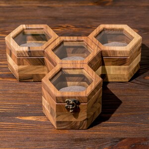 K&ouml;nnte beinhalten: Eine sechseckige Holzkiste mit f&uuml;nf F&auml;chern, jedes mit einem Glasdeckel. Die Kiste ist aus verschiedenen Holzsorten gefertigt, die ein einzigartiges Muster bilden. Die Kiste ist perfekt zum Aufbewahren von kleinen Gegenst&auml;nden wie Schmuck oder Uhren.
