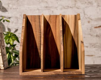May include: Wooden desk organizer with three vertical compartments. The organizer is made of light brown wood with visible grain patterns. The design is simple and functional, suitable for office or home use.