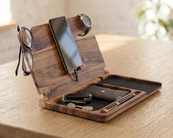 May include: A wooden valet tray with compartments for everyday carry items. The tray holds a smartphone, glasses, a watch, keys, a wallet, and a pen. The wood has a rich, dark brown color.