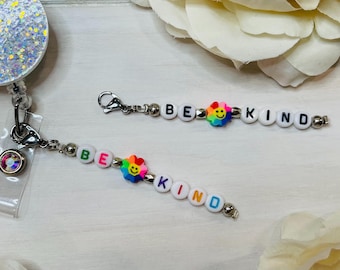 May include: Two white beaded necklaces with silver clasps and rainbow flower charms. The beads spell out "BE KIND".