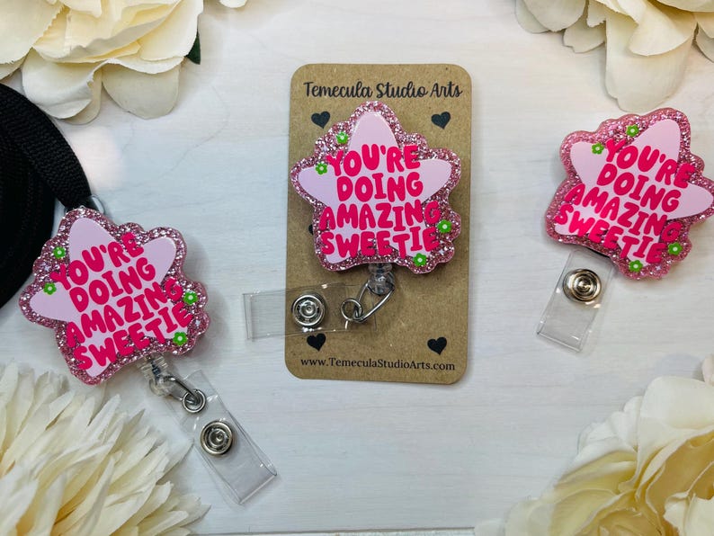 May include: Pink star-shaped badge holder with a glitter finish and the text "You're doing amazing sweetie".