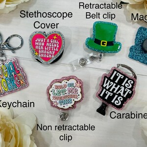 May include: A collection of accessories including a keychain, stethoscope cover, retractable belt clip, magnet, non-retractable clip, and carabiner. The keychain reads "SOCIAL WORKER". The stethoscope cover is heart-shaped and says "JUST A GIRL WHO NEEDS HER LITTLE SNACKY SNACKS".