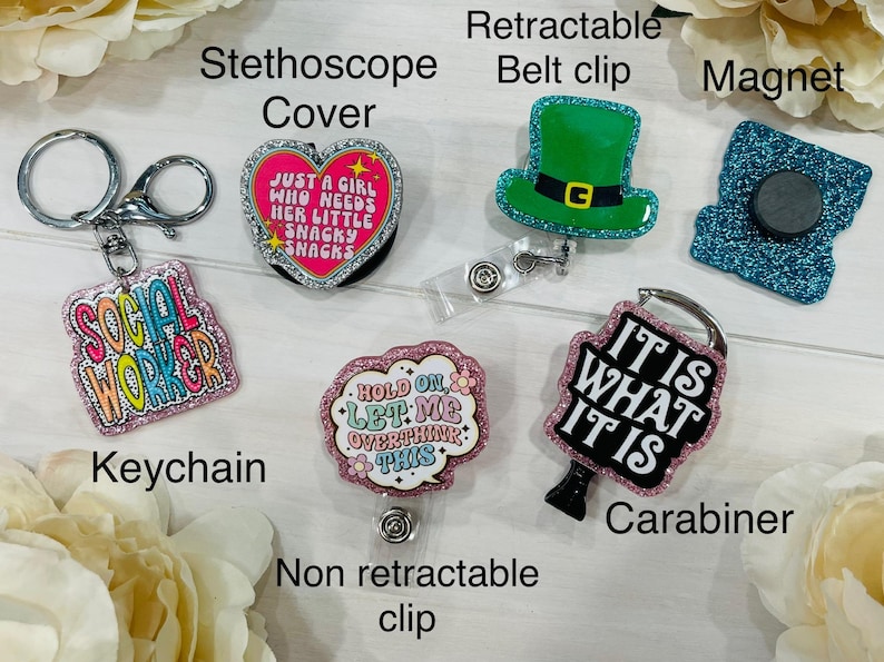 May include: A collection of accessories including a keychain, stethoscope cover, retractable belt clip, magnet, non-retractable clip, and carabiner. The keychain reads "SOCIAL WORKER". The stethoscope cover is heart-shaped and says "JUST A GIRL WHO NEEDS HER LITTLE SNACKY SNACKS".