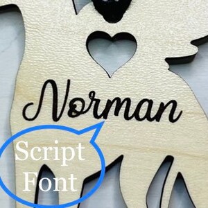 Op de afbeelding: Houten engel ornament met een hartvormige uitsparing en de naam "Norman" geschreven in een schrijfletter.