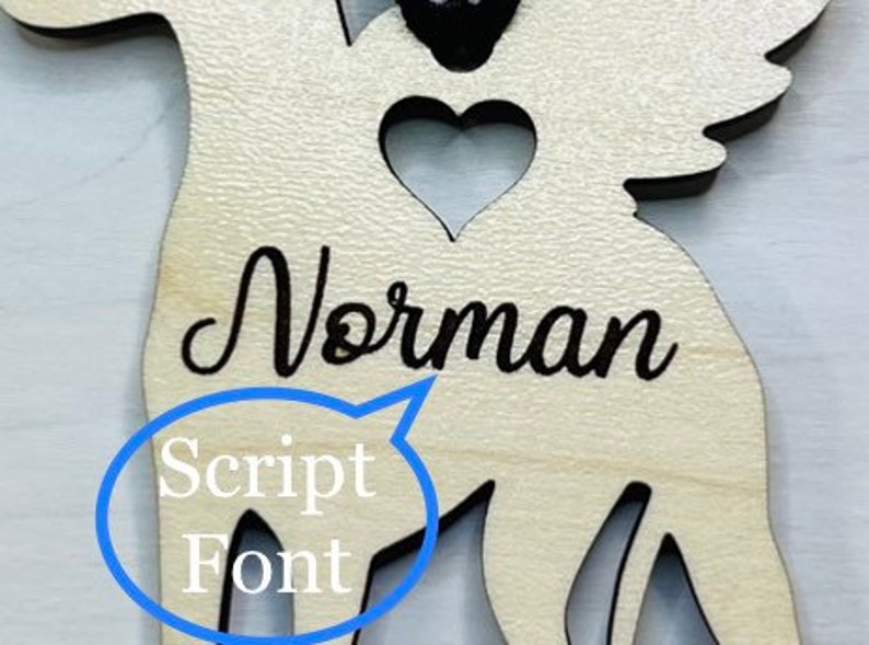 Op de afbeelding: Houten engel ornament met een hartvormige uitsparing en de naam "Norman" geschreven in een schrijfletter.