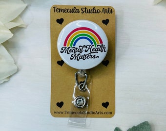 May include: A white button with a rainbow and the text "Mental Health Matters" on it. The button is attached to a retractable badge holder with a silver clip.