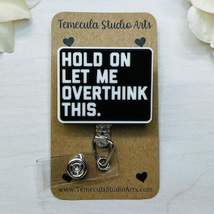 May include: Black and white badge holder with a black background and white text that reads "Hold on let me overthink this." The badge holder is attached to a silver retractable badge reel.
