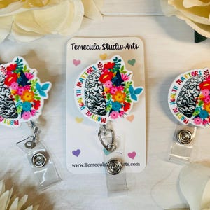 May include: Three white badge reels with a colorful brain design and the text "Mental Health Matters".