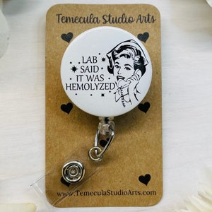 May include: White round badge holder with a black and white illustration of a woman on the phone. The text on the badge reads "Lab said it was hemolyzed".