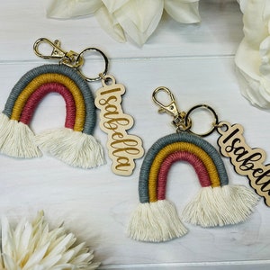 May include: Two rainbow-colored keychains with wooden tags that say "Isabella". The keychains are made of yarn and have white tassels.