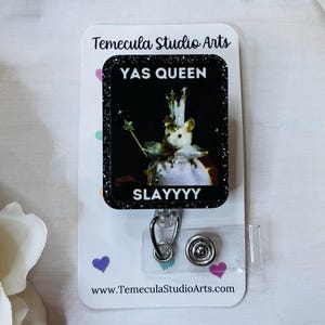 K&ouml;nnte beinhalten: Ein Ausweis-Rollhalter mit einem schwarzen Glitzerrahmen, der eine Maus zeigt, die als K&ouml;nigin mit Krone und Zauberstab gekleidet ist. Der Text "YAS QUEEN SLAYYYY" ist auf dem Ausweis zu sehen. Die Rolle ist an einer wei&szlig;en Karte mit dem Logo von Temecula Studio Arts befestigt.