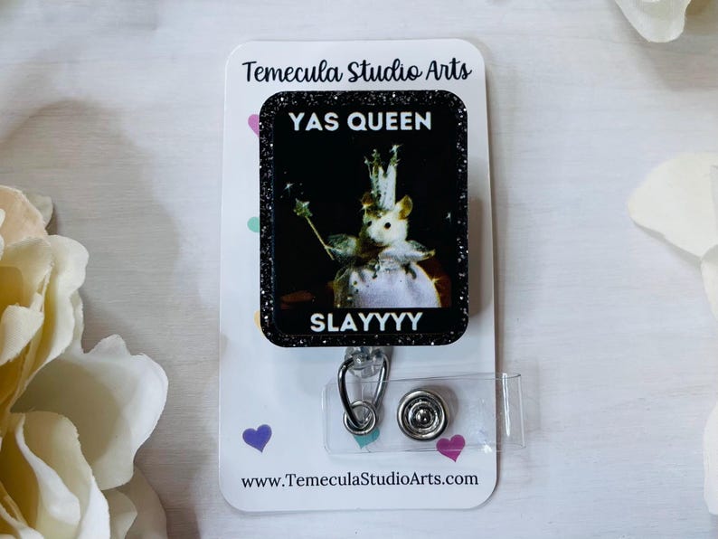 K&ouml;nnte beinhalten: Ein Ausweis-Rollhalter mit einem schwarzen Glitzerrahmen, der eine Maus zeigt, die als K&ouml;nigin mit Krone und Zauberstab gekleidet ist. Der Text "YAS QUEEN SLAYYYY" ist auf dem Ausweis zu sehen. Die Rolle ist an einer wei&szlig;en Karte mit dem Logo von Temecula Studio Arts befestigt.