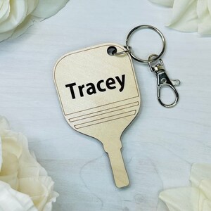 May include: A wooden paddle keychain with the name "Tracey" engraved on it. The keychain is attached to a silver metal key ring.