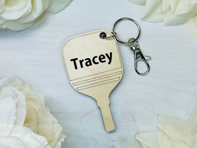 May include: A wooden paddle keychain with the name "Tracey" engraved on it. The keychain is attached to a silver metal key ring.