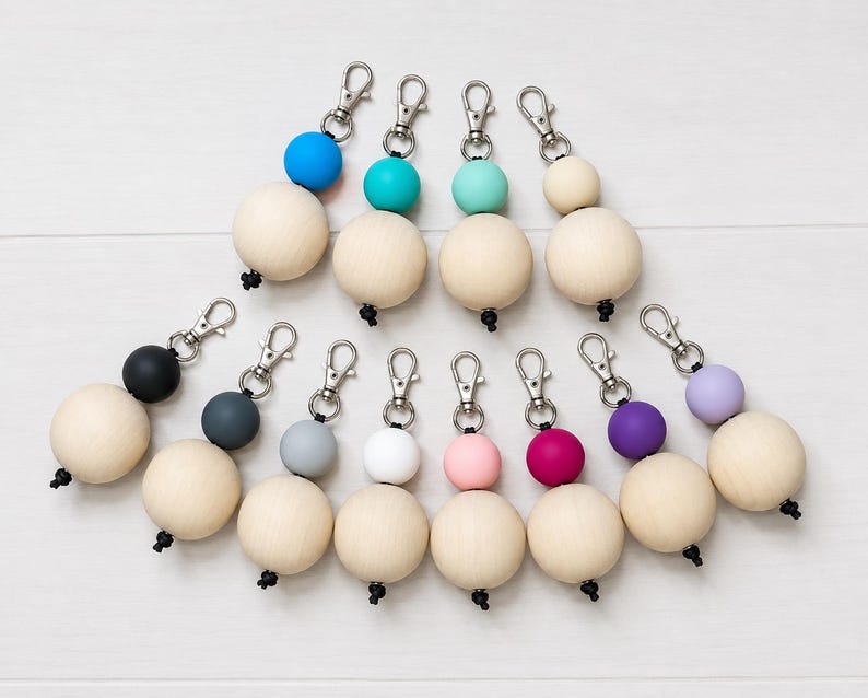 Puede incluir: Una colecci&oacute;n de llaveros con cuentas de madera y cuentas de acento de colores, incluyendo azul, turquesa, rosa, morado y negro. Cada llavero tiene un cierre plateado.