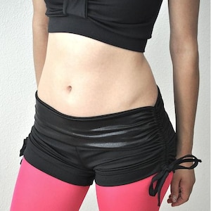 May include: Black and pink dance shorts with a drawstring detail. The shorts are made of a shiny, stretchy fabric.