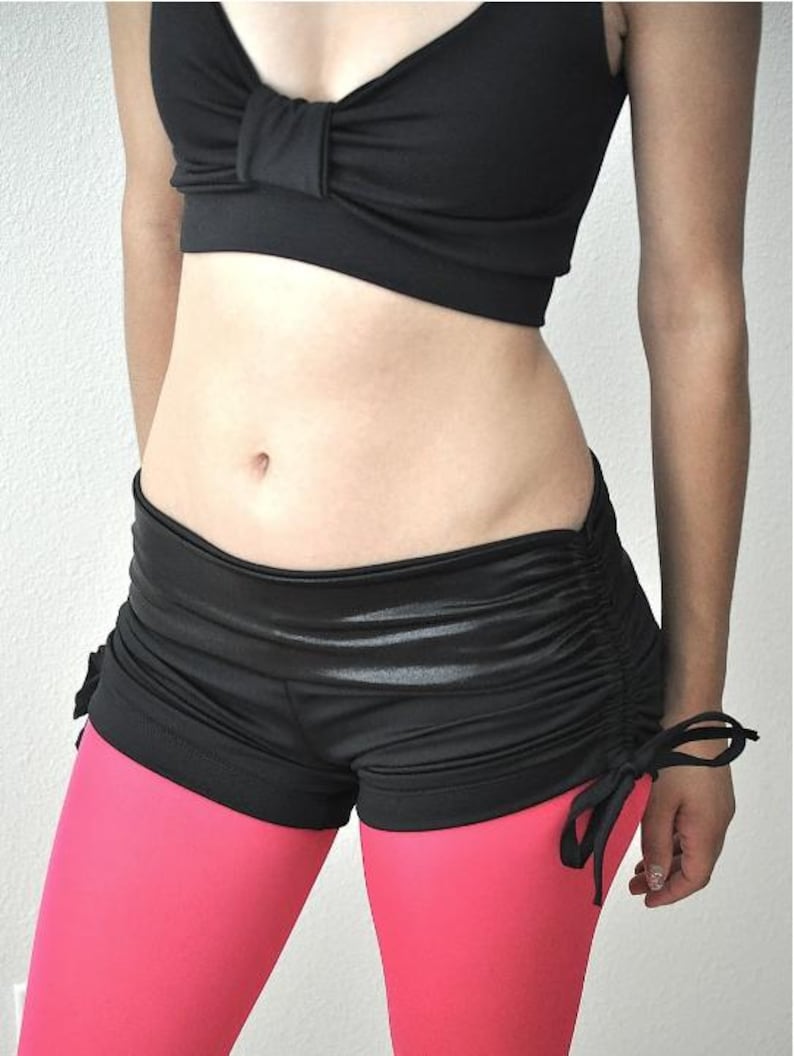 May include: Black and pink dance shorts with a drawstring detail. The shorts are made of a shiny, stretchy fabric.