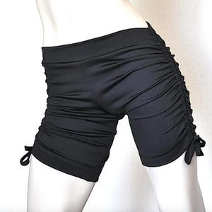 May include: Black athletic shorts with a drawstring detail on the sides. The shorts are made of a stretchy, comfortable fabric.