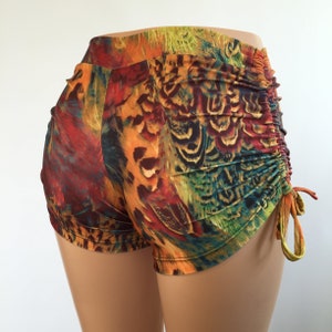 May include: High-waisted shorts featuring a vibrant, multi-colored abstract print in shades of red, orange, yellow, and teal. The garment includes a gathered, ruched side detail with adjustable drawstring ties that create a textured, fitted appearance.