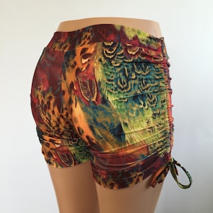May include: Shorts featuring a vibrant, multicolored feather print in shades of orange, red, yellow, and green. The garment has a high waistband and side-seam ruching with adjustable drawstring ties at the bottom hem, creating a gathered effect.