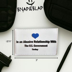 Puede incluir: Un parche rectangular blanco con el texto "In an Abusive Relationship With The U.S. Government Today" y un corazón azul. El parche mide 7,6 cm de ancho y 4,76 cm de alto. La imagen también incluye el texto "SNAP&SLAP".