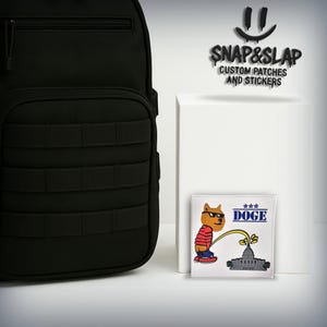 May include: A black backpack with a tactical design is next to a white square. A square sticker features a cartoon dog wearing sunglasses, urinating on a building, with the word "DOGE". The text "SNAP&SLAP CUSTOM PATCHES AND STICKERS" is above.