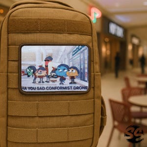 Könnte beinhalten: Ein beigefarbener taktischer Rucksack mit einem rechteckigen Aufnäher mit einem Cartoon-Bild von Figuren vor einem Geschäft. Der Aufnäher hat den Text "HA YOU SAD CONFORMIST DRONE" unten.