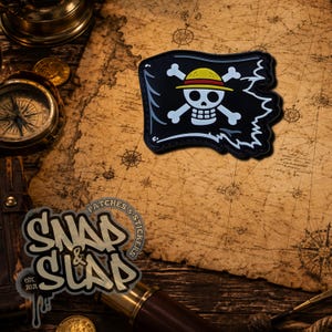 May include: A black rectangular patch with a tattered edge design featuring a white skull and crossbones wearing a yellow straw hat with a red band. The patch is displayed on a vintage-style map background with a compass and a telescope nearby.