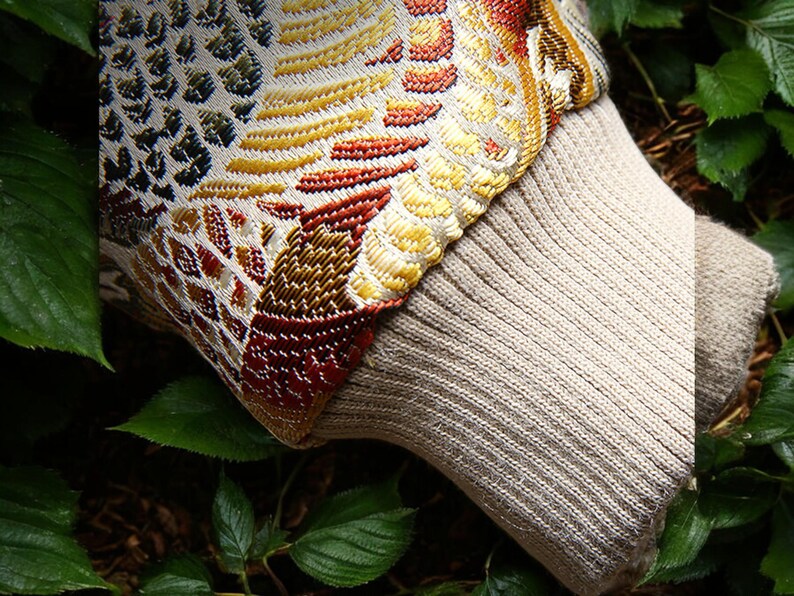 May include: A close-up of a beige knitted fabric with a colorful patterned trim. The fabric is textured and has a ribbed appearance. The trim features a geometric design with shades of red, yellow, green, and blue.