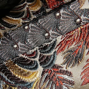 May include: Close-up of a fabric with an intricate embroidered design. The fabric features a variety of colors, including gold, red, brown, and blue. The design is made up of leaves and flowers.