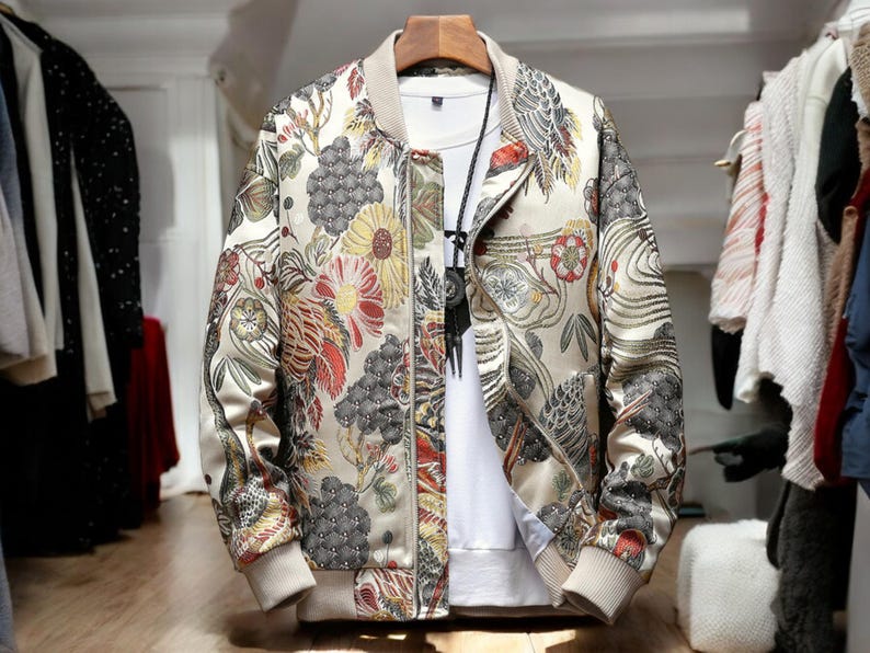 May include: A beige bomber jacket with a floral print featuring a variety of colors, including red, yellow, and green. The jacket has a zipper closure and a ribbed collar.