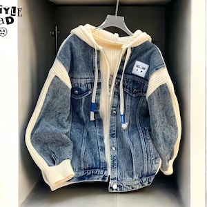 May include: A blue denim jacket with a cream-coloured knit hood and sleeves. The jacket has a button-up front and a small patch on the chest. The text "ALL STYLE SQUAD" is visible on the upper left.