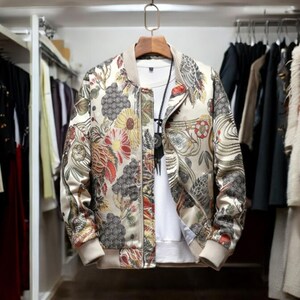 May include: A beige bomber jacket with a floral print featuring red, yellow, and green flowers. The jacket has a zipper closure and a ribbed collar, cuffs, and hem.